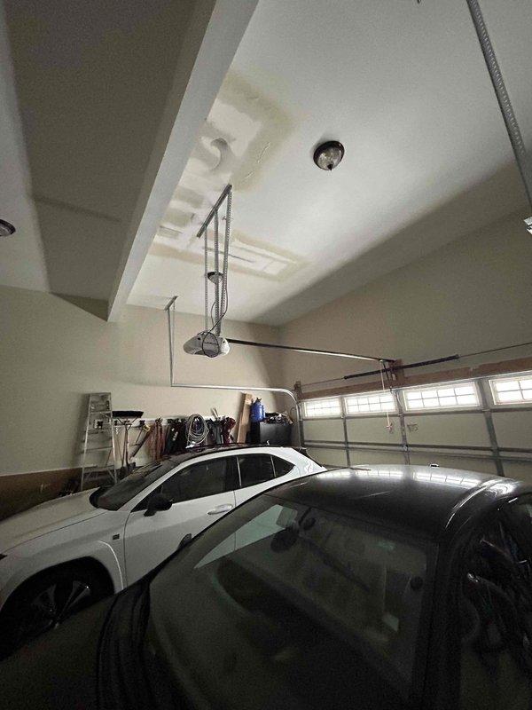 Responded to water leak emergency in garage ceiling caused by customer's use of space heater in room above garage during suspected pipe freeze. Visual inspection revealed water stains on garage ceiling and confirmed flooding had occurred but active leaking had stopped. Documented damage with photos showing affected ceiling area above two parked vehicles and adjacent storage.