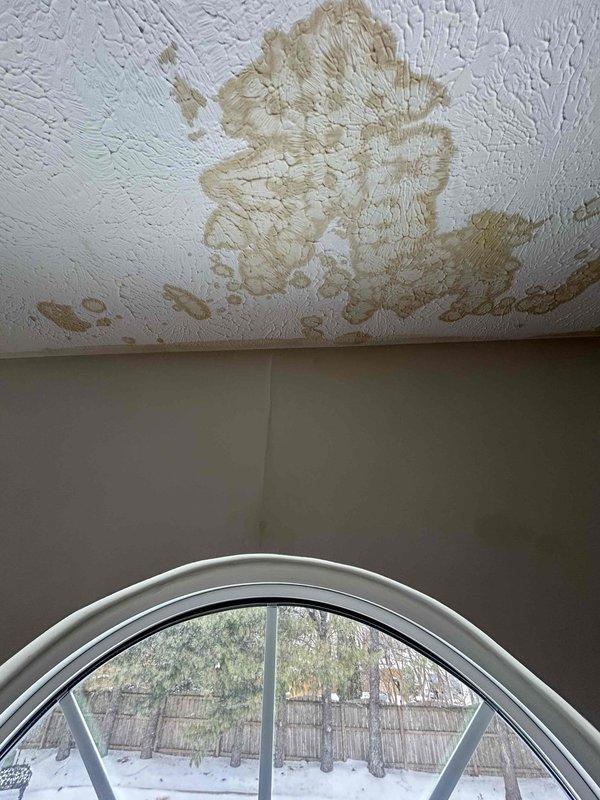 Responded to water leak service call. Identified significant water damage on ceiling below attic-mounted air handler. Observed spreading brownish stains on textured ceiling and inspected air register for potential condensate line blockage or pan overflow. Remediated leak source and advised customer on necessary ceiling repairs.