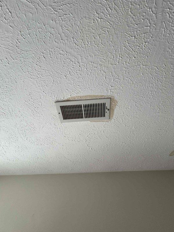 Responded to water leak service call. Identified significant water damage on ceiling below attic-mounted air handler. Observed spreading brownish stains on textured ceiling and inspected air register for potential condensate line blockage or pan overflow. Remediated leak source and advised customer on necessary ceiling repairs.