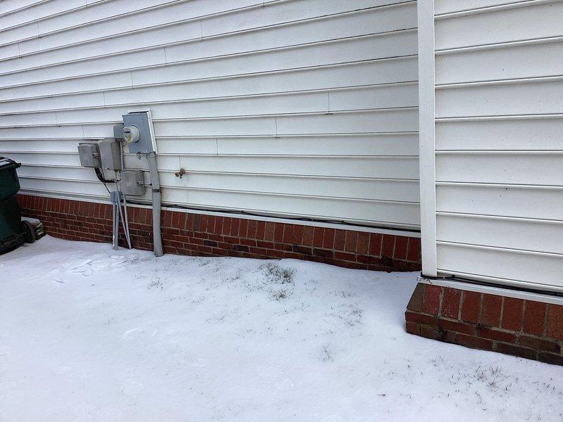 Conducted on-site assessment for generator installation at residential property. Evaluated existing electrical service entrance components, including utility meter and junction boxes. Documented current electrical setup and mounting conditions on exterior wall with white horizontal siding and brick foundation for proper generator integration planning.