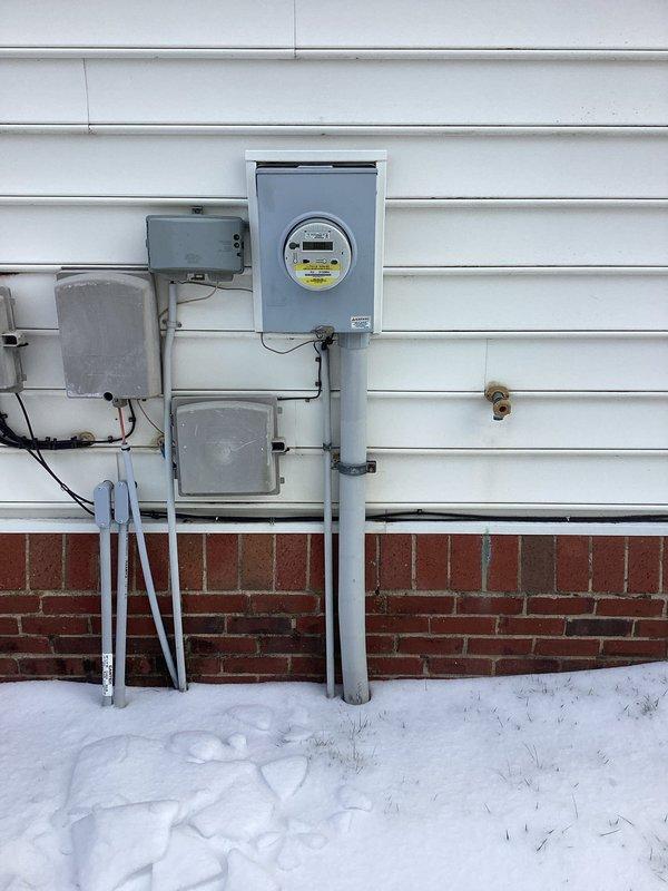 Conducted on-site assessment for generator installation at residential property. Evaluated existing electrical service entrance components, including utility meter and junction boxes. Documented current electrical setup and mounting conditions on exterior wall with white horizontal siding and brick foundation for proper generator integration planning.