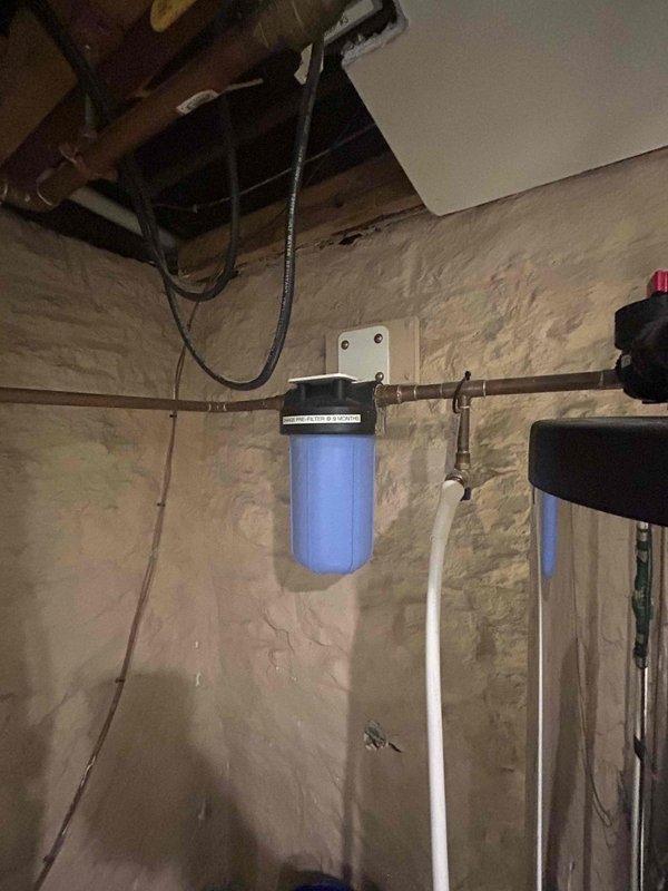 Diagnosed and replaced clogged whole-house water filtration system causing loss of pressure throughout the residence. Inspection revealed a severely fouled pre-filter in the main blue canister unit mounted on copper supply lines, restricting water flow. After replacement, system restored to normal operating pressure.