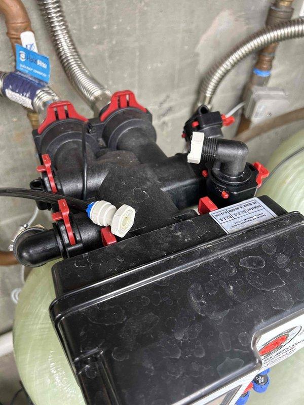 Responded to service call for water leak from a water softener tank causing air in lines. Diagnosed leaking manifold system with multiple connection points showing moisture accumulation. Replaced faulty circular metal connector component and restored proper function to water distribution system, eliminating both the leak and air infiltration issues.