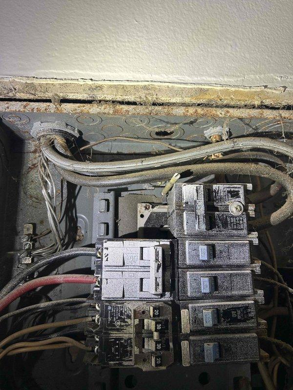 Conducted evaluation of outdated residential electrical panel showing significant dust accumulation, exposed insulation where panel meets wall, and improper wiring configuration. Panel requires complete replacement due to age-related deterioration, safety concerns from dust buildup on circuit breakers, and non-compliant installation with visible gaps between electrical box and wall surface.