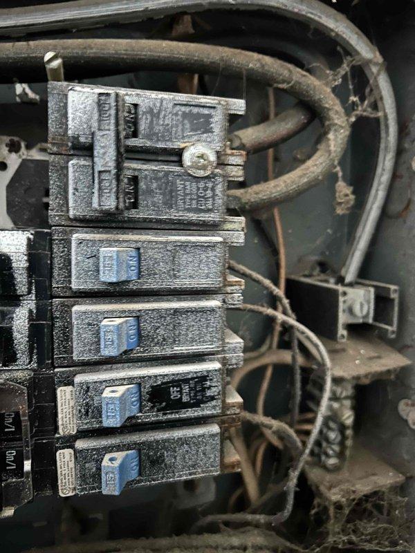 Conducted evaluation of outdated residential electrical panel showing significant dust accumulation, exposed insulation where panel meets wall, and improper wiring configuration. Panel requires complete replacement due to age-related deterioration, safety concerns from dust buildup on circuit breakers, and non-compliant installation with visible gaps between electrical box and wall surface.