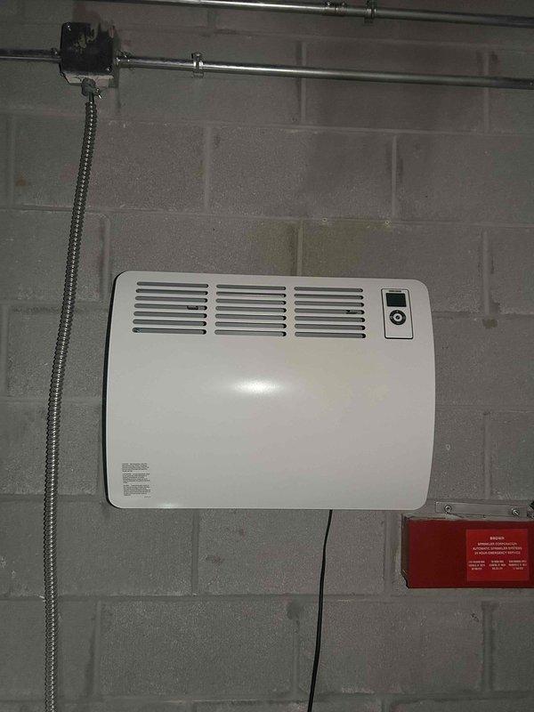 Successfully replaced outdated wall-mounted space heater with new CON 150-2 Premium wall-mounted electric convection heater on concrete block wall. Unit was properly mounted, connected to existing electrical supply via junction box, and tested for proper operation. Photographic documentation of completed installation was taken showing proper placement and functionality of new heating system.