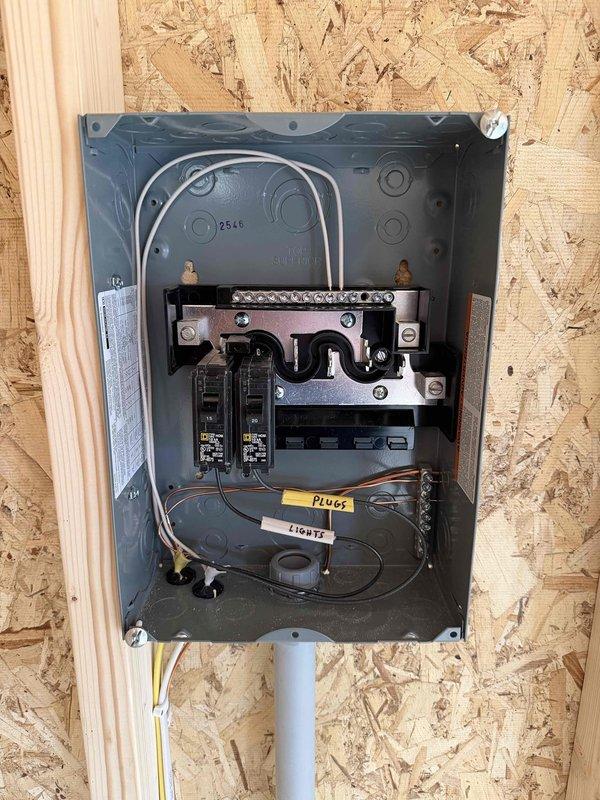 Completed installation of a 100 AMP electrical panel with two circuit breakers in a wooden framed structure during construction phase. Installed one GFCI outlet, two duplex receptacles, one single pole switch, and three keyless fixtures, with proper labeling for plug and lighting circuits. All components were securely mounted to OSB wall with appropriate wiring and conduit connections according to electrical code requirements.