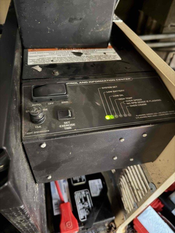 Performed routine maintenance on a Generac residential generator located under wooden patio behind house. Inspected control panel which showed normal operation with AUTO mode engaged and no warning indicators illuminated. Noted generator environment contained significant leaf debris accumulation around unit and battery, requiring cleaning to maintain proper ventilation and prevent potential fire hazards.