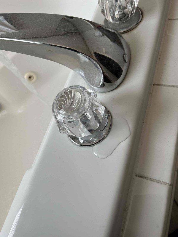 Conducted a plumbing inspection focusing on sink installation, noting oxidation and corrosion on copper/brass valves with improvised foil tape connections at joints. Observed water leakage at the base of the crystal handle faucet as evidenced by standing water on the sink surface.