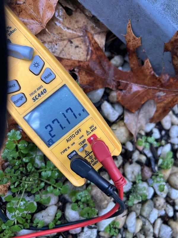 Diagnosed 5-year-old AC system that was blowing cold air. Multimeter testing revealed significantly low capacitance (27.17μF) on the dual run capacitor (30+5μF), which showed visible deterioration and dust accumulation. Replaced failing capacitor and cleaned debris from unit to restore proper cooling operation.