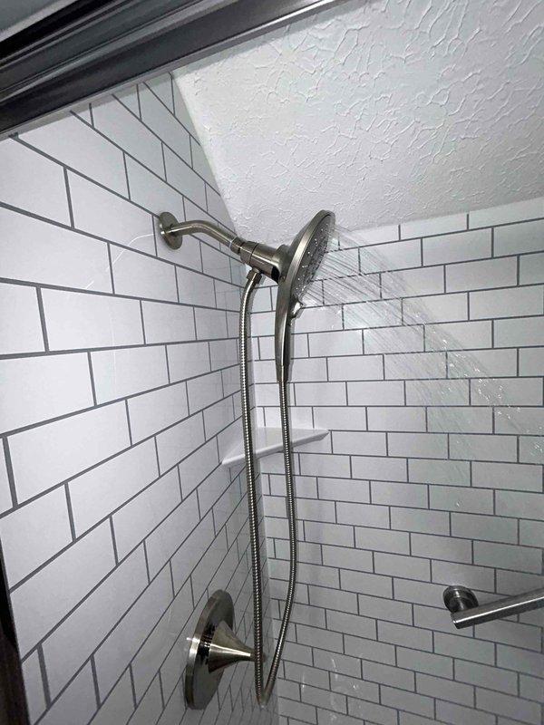Completed routine plumbing inspection of bathroom fixtures with focus on shower installation and toilet connections. Examined shower system components including diverter valve, fixed showerhead, and handheld unit, all in working order. Noted minor corrosion on toilet supply line connection at wall penetration that should be monitored but currently maintains proper seal with no active leaks detected.