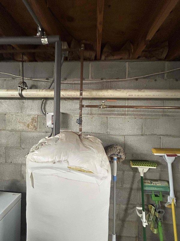Conducted inspection of existing 50-gallon electric water heater located in basement utility area. Unit shows signs of aging with partial insulation wrap and standard pressure relief valve setup. Documented current installation configuration including electrical connections (240V) and plumbing infrastructure with copper supply lines. Provided estimate options for replacement of equivalent electric tank model versus tankless alternatives.