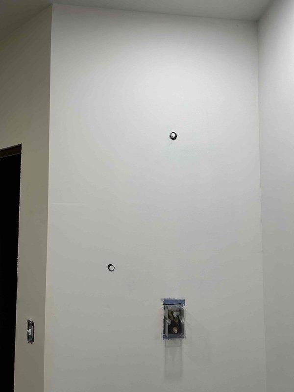 Completed plumbing estimate for bathroom rough-in with two sets of hot/cold water supply lines protruding from the wall, marked with appropriate color indicators. Observed electrical work in progress with multiple outlet boxes installed and noted preparation for future fixture installations including two circular wall cutouts requiring coordination with electrical components.