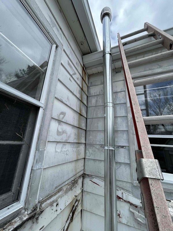 Removed non-compliant water heater vent pipe hanger that was improperly attached to gutter and installed proper support per code requirements. This correction allows customer's gutter maintenance to proceed without obstruction while ensuring exhaust system remains securely anchored to structure.