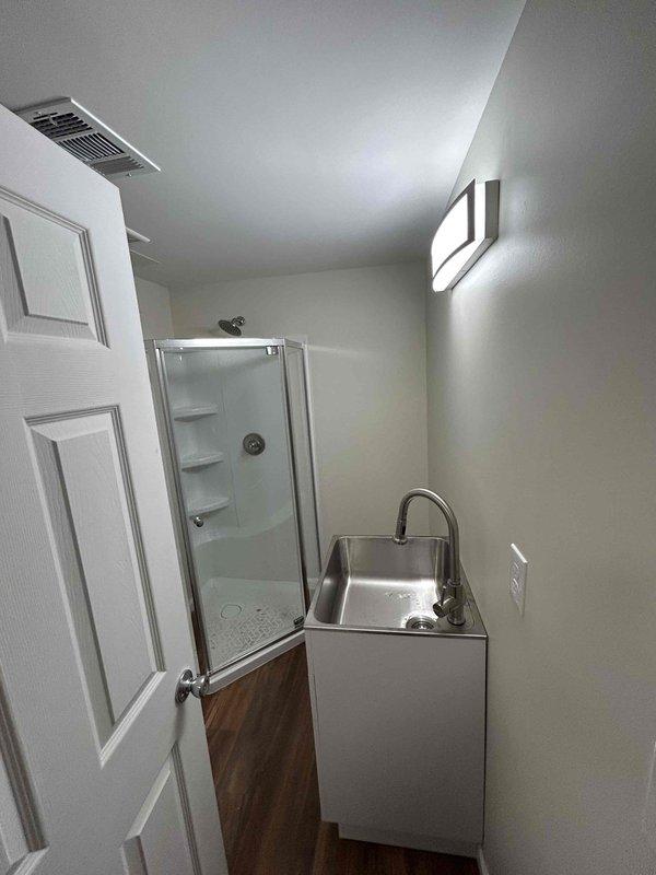 Completed final phase of utility room installation, including connection and mounting of stainless steel sink with chrome faucet to the metal cabinet, as well as installation of shower stall fixtures including ceiling-mounted showerhead and wall-mounted water control handle. All plumbing connections were properly sealed and tested for functionality after drywall, painting, and flooring work had been completed by others.