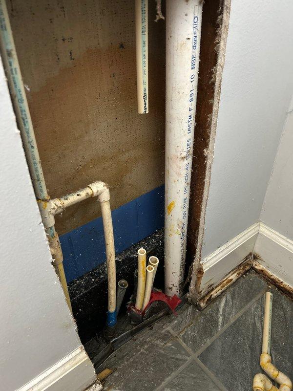 Responded to service call regarding water leak between shower and wall on concrete slab foundation. Upon inspection, removed drywall section to access plumbing components, revealing multiple PVC pipes with water supply lines and evidence of moisture damage. Identified leak source at PEX tubing connection points with metallic fittings, performed necessary repairs to resolve the water intrusion issue.
