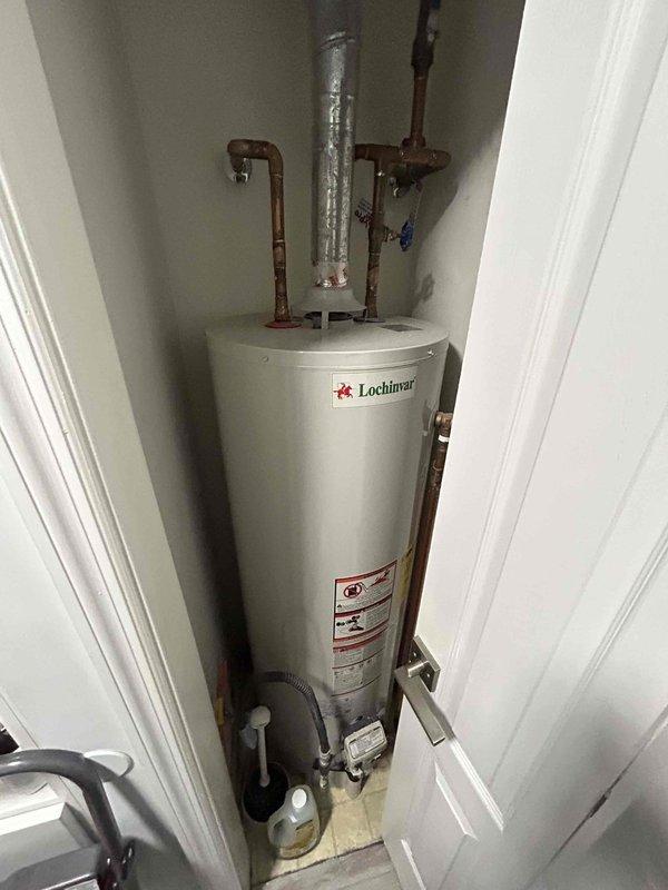 Conducted assessment for tank to tankless water heater replacement. Current installation includes Lochinvar tank water heater installed in utility closet with copper supply lines showing age-related patina and possible moisture issues at base. Evaluated attic space for potential tankless installation, noting adequate structural support, existing ductwork, and electrical access. Customer will supply new tankless unit; quote provided for professional installation services.