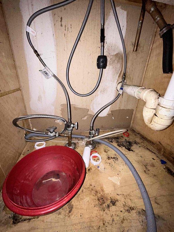 Conducted on-site assessment for kitchen sink installation. Observed existing double-basin sink with significant water damage and possible mold in the cabinet below. Noted deteriorated wooden cabinet floor with water collection basin present, suggesting ongoing leak issues. Examined current plumbing configuration including braided supply lines and PVC drainage components for replacement planning.