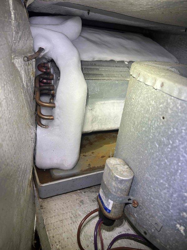 Responded to no cooling complaint on 15-year-old electric heat pump system located in attic space above home addition. Upon inspection, found air handler blowing ambient temperature air with no refrigerant cooling. Accessed indoor unit compartment and discovered severely deteriorated evaporator coil insulation that had expanded and separated from coil assembly, indicating prolonged moisture exposure and potential refrigerant leak. Observed copper refrigerant lines with oxidation and filter drier showing signs of age-related degradation. Documented equipment condition with photographs showing compromised insulation material, evaporator coil assembly, and refrigerant line connections. Given the age of the system and extent of component deterioration, provided customer with diagnostic findings and repair options including coil replacement versus full system replacement recommendations.