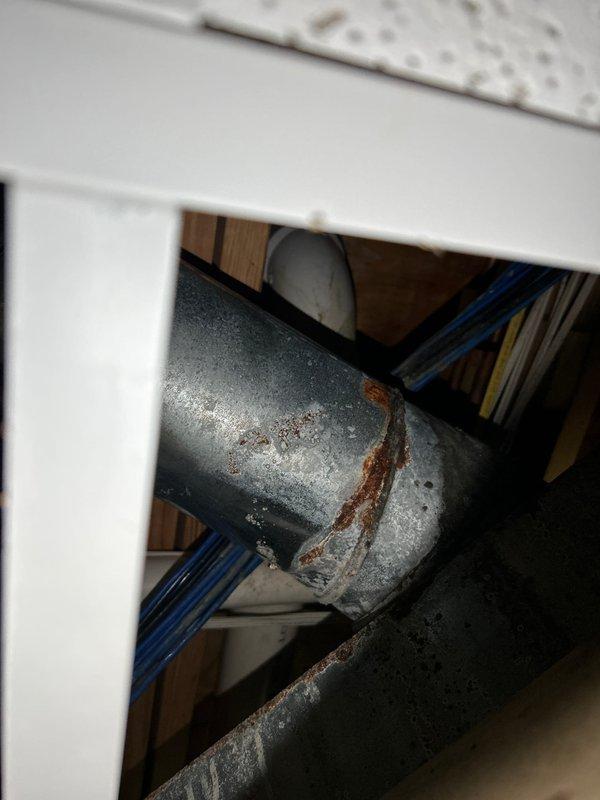 Responded to plumbing service call for multiple leak issues in a 26-year-old residential property. Located and inspected leaking copper pipe running through floor/ceiling cavity between structural levels, documenting significant corrosion and rust deterioration on galvanized metal components with visible moisture staining and mineral deposits. Investigated reported kitchen sink leak, identifying actual source as separate issue beneath sink rather than sink fixture itself. Accessed confined structural space containing multiple utility systems including copper water lines, PVC drainage, and various conduits to assess extent of pipe deterioration and water damage. Photographed corroded sections showing compromised galvanized coating and active moisture infiltration points for repair documentation and quote preparation.