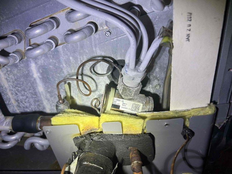 Responded to no cooling complaint on 7-year-old electric furnace and air conditioning system with air handler located in attic. Upon inspection, found system blowing room temperature air with no refrigerant circulation. Accessed interior components of air handler and outdoor condensing unit to perform diagnostic evaluation. Identified accumulation of dust and debris on interior panels indicating inadequate filtration and possible airflow restrictions. Inspected evaporator coil assembly, refrigerant lines, condensate drainage system, and electrical connections. Documented condition of gas valve assembly, control board, and associated wiring harnesses. Photographed interior components showing yellow insulated suction line, copper refrigerant piping, and cabinet conditions for service records and further assessment of cooling system failure.