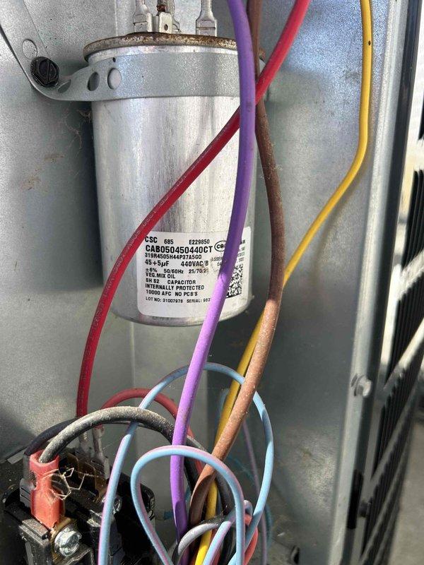 Responded to no cooling complaint on electric heat pump system. Upon arrival, thermostat displayed 70.5°F setpoint but system was not achieving temperature. Performed diagnostic inspection of indoor air handler unit located near entry door. Visually inspected electrical components including dual run capacitor and associated wiring connections. Examined capacitor terminals, control wiring (red, purple, yellow, blue, and orange conductors), and terminal block connections for signs of failure or degradation. Documented system conditions with photographs of thermostat display and internal electrical components for service records.