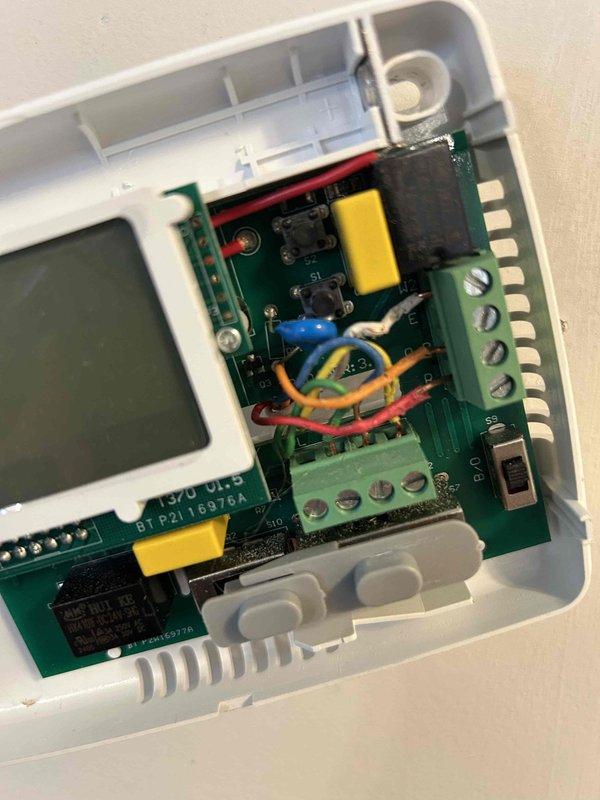 Responded to no heat call on older electric HVAC system located in second bedroom with reported breaker tripping issues. Upon arrival, performed diagnostic evaluation of thermostat and control system. Inspected wall-mounted thermostat unit, removed cover to access internal components and circuit board. Examined wiring connections, LCD display functionality, capacitor, relay, and terminal block connections for signs of electrical faults or component failure that could cause breaker trips. Documented internal condition of thermostat PCB and wiring configuration with photographs for service records.