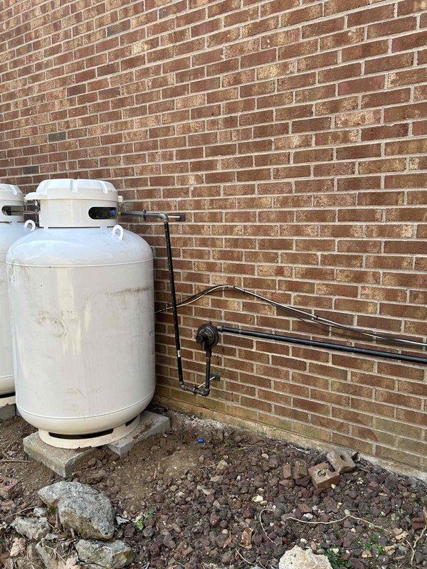 Completed gas piping installation for generator system, running LP gas line from propane tank regulator to generator connection point. Installed black gas piping with proper mounting hardware along exterior brick wall, ensuring secure attachment and code-compliant routing. Documented tile work repairs needed for property owner's contractor coordination.