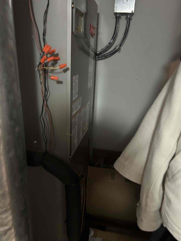 Responded to no cooling call on 1-year-old electric HVAC system displaying system alert at thermostat. Upon arrival, found air handler installed in laundry room with multiple replacement filters staged nearby. Performed diagnostic evaluation of indoor unit and electrical connections. Inspected wire terminations at unit with orange wire nuts visible at top connections. Verified filter had been changed approximately one month prior. System alert condition preventing cooling operation was addressed, restoring normal functionality to the air conditioning system.