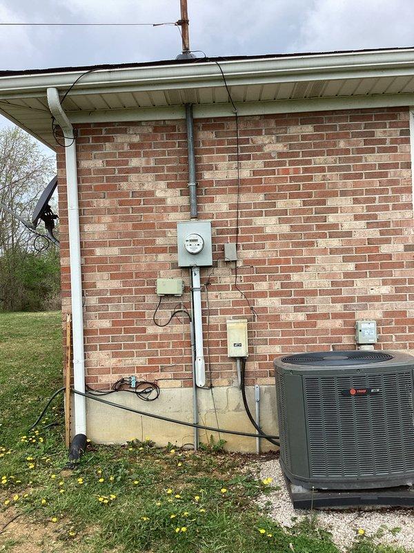 Conducted comprehensive electrical site assessment for backup generator installation at brick building. Evaluated existing electrical infrastructure including current meter location, service entrance configuration, and main distribution panel capacity. Documented exterior mounting locations for transfer switch and generator pad placement near existing HVAC equipment on gravel base. Assessed interior electrical panel with dual-row circuit breaker arrangement to determine integration requirements for automatic transfer switch installation. Photographed existing conduit routing and service entrance components to develop accurate material list and labor estimate for generator interconnection project.