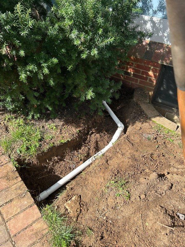 Disconnected sump pump discharge line from the sanitary sewer system to bring installation into compliance with code requirements. Cored a penetration through the foundation wall and installed approximately 15 feet of PVC discharge piping extending from the basement to the backyard discharge point. Excavated trench through existing brick pathway in backyard, removed necessary pavers to accommodate underground piping, and routed discharge line away from the foundation to proper termination point. Installed new interior PVC piping with proper fittings and connections to redirect sump pump flow through the foundation wall. Backfilled excavated areas and reset brick pavers along pathway to restore access, prioritizing functionality of the discharge system.