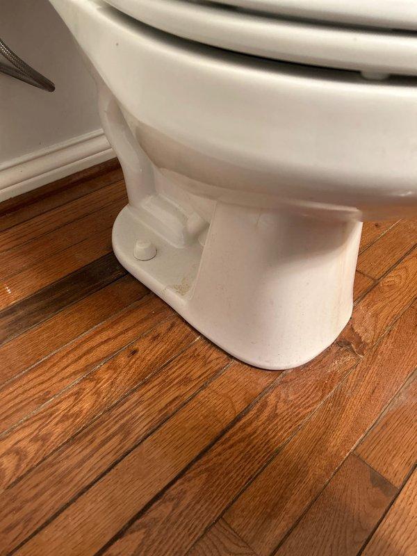 Performed routine plumbing inspection of toilet system, examining internal tank components including fill valve assembly, flush valve mechanism, flapper chain, and refill tube connections. Documented mineral buildup and water staining throughout tank interior, and verified proper installation and structural condition of toilet base and floor mounting.