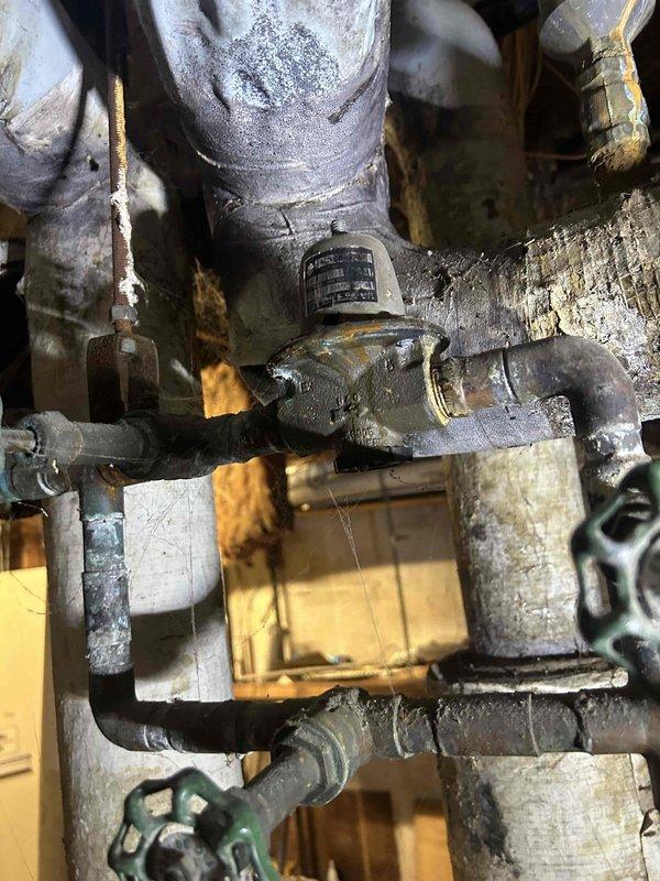 Responded to no-heat service call for boiler system that had been non-operational since property acquisition. Upon arrival, performed diagnostic inspection of boiler and associated piping infrastructure. Documented existing conditions including deteriorated pipe connections, corroded brass fittings with mineral deposits, and aging plumbing components showing significant wear. Assessed central cylindrical boiler component and surrounding pipe configuration with multiple joints and connections. Identified corrosion and discoloration on metal surfaces throughout the system. Photographed critical areas including compromised pipe unions and fittings requiring attention for proper system operation and safety compliance.