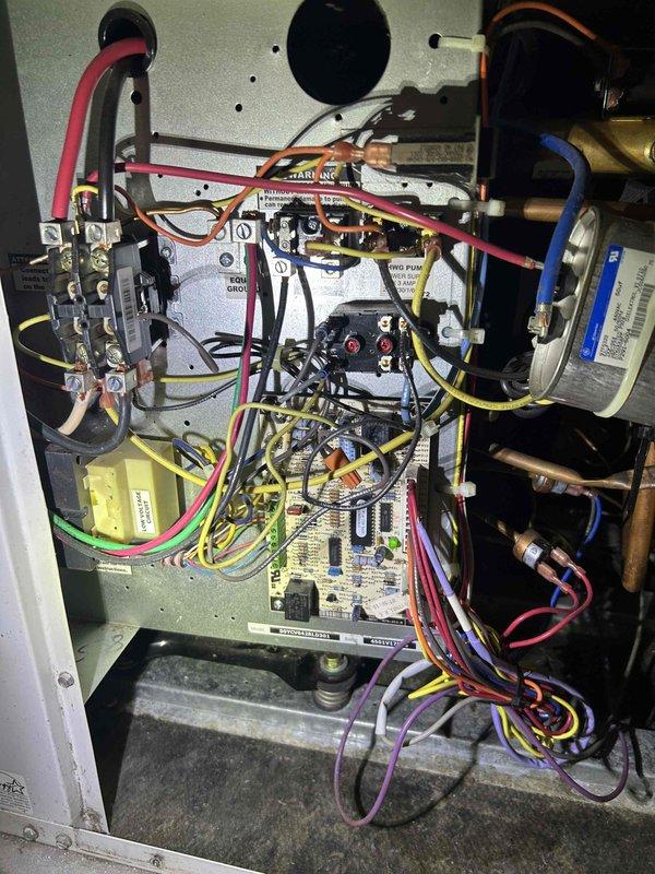 Responded to no-cool service call on 20-year-old geothermal HVAC system located in basement laundry room. Upon arrival, assessed system damage following major water leak incident that had previously tripped the main breaker. Conducted comprehensive diagnostic evaluation of geothermal unit's internal components, including inspection of circuit board, electrical contactors, relays, wiring harness, and refrigerant line connections. Removed access panel and documented condition of all electrical and mechanical components, noting dust accumulation and operational wear throughout control compartment. Inspected copper refrigerant lines with brass fittings for potential water damage or corrosion. Evaluated basement ductwork system for water intrusion and structural damage. Photographed internal unit components showing circuit board assembly, colored wiring connections (red, blue, yellow, purple, white), contactors with copper connection points, and associated mechanical assemblies. Documented 