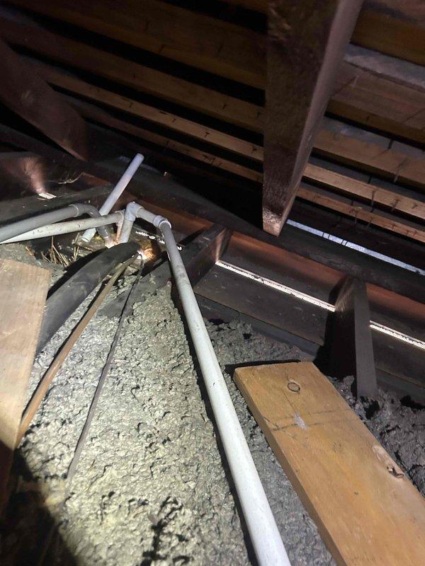 Responded to callback for water leak originating from HVAC piping in attic space following recent service work. Upon arrival, documented extensive water damage and staining on bedroom ceiling with discoloration following ceiling panel seams. Accessed attic space and inspected PVC condensate drain lines running through insulated area above affected room. Located active leak at pipe connection point near previous repair site. Identified improper fitting installation as source of water intrusion causing ceiling damage below. Repaired faulty connection, secured all pipe sections, and verified proper drainage operation. Confirmed no additional leaks present and system operating correctly.