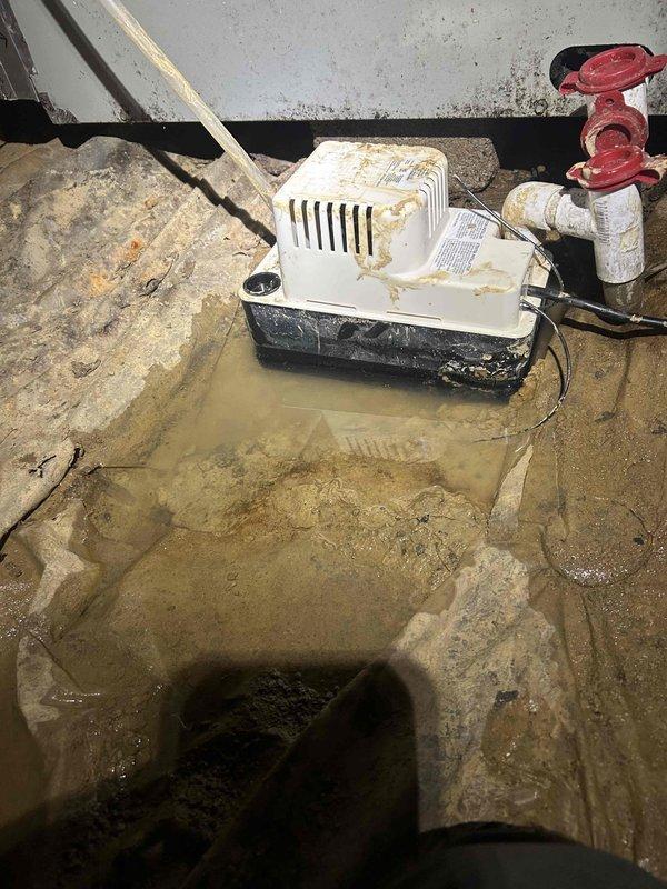 Responded to service call regarding chemical odor in bedroom during air conditioning operation. Upon inspection, discovered condensate pump in crawl space with standing water accumulation on concrete floor, indicating drainage issues. Examined exterior drainage system and downspout configuration at foundation level. Chemical smell determined to be related to stagnant water in condensate system causing biological growth and odor transmission through HVAC ductwork. Documented moisture conditions and drainage components for recommended corrective action.