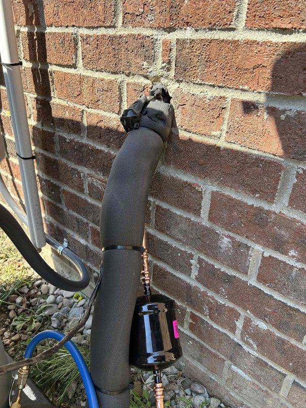 Completed full residential heat pump system installation including Bryant 2.5 ton 14.3 SEER2 heat pump outdoor unit (model GH5SAN53000A), Bryant 2.5 ton air handler (model FJ5ANXB30L10), and Bryant 10KW electric heat kit (model TU-EC-10BKB). Installed Honeywell digital thermostat for system control. Mounted outdoor unit on concrete pad with snow legs for elevation and proper drainage. Installed electrical disconnect box and whip kit at outdoor unit location. Ran insulated refrigerant lines from outdoor unit to attic-mounted air handler, secured along exterior brick wall with proper mounting hardware. Installed refrigerant line filter drier for system protection. Positioned air handler horizontally between attic joists with proper support and clearances. Connected black flexible insulated ductwork to air handler and integrated with existing duct system using custom transitions. Installed standard-sized air filter rack for maintenance access. Added SS2 coil drain safety water sensor and 