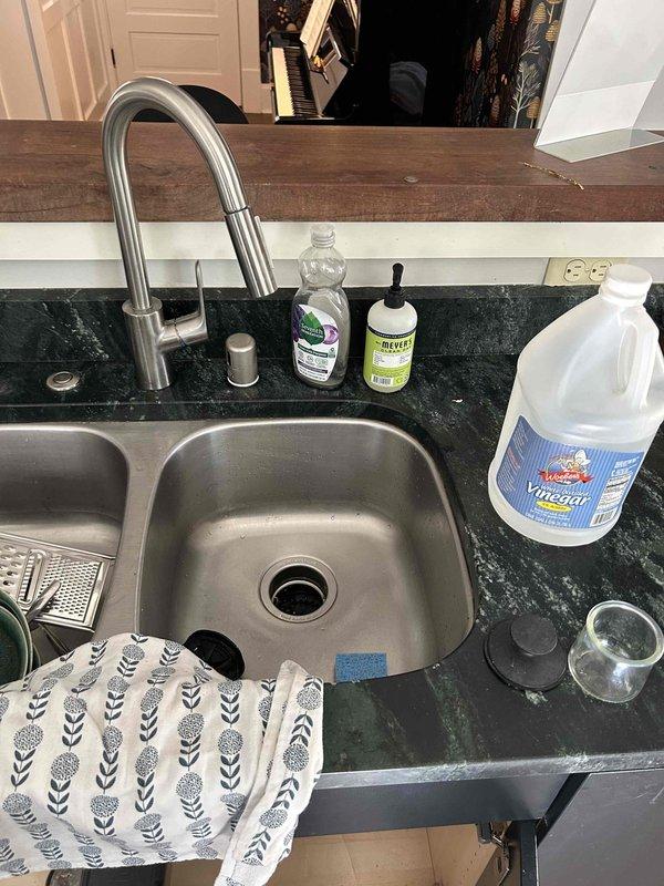 Responded to service call for steady water leak in basement with associated odor and leak under kitchen sink. Upon arrival, conducted visual inspection of kitchen sink drain assembly and P-trap configuration. Examined chrome drain basket, white PVC P-trap, compression fittings, and horizontal drain line for signs of active leakage or deterioration. Inspected braided supply lines, garbage disposal connections, and all visible plumbing components under sink for moisture, corrosion, or loose fittings. Documented existing plumbing configuration including standard residential drainage setup with white plastic fittings. Assessed basement area for source of water intrusion and odor. No drainage blockages or backup conditions were observed during inspection.