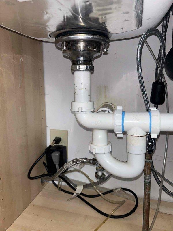 Responded to service call for steady water leak in basement with associated odor and leak under kitchen sink. Upon arrival, conducted visual inspection of kitchen sink drain assembly and P-trap configuration. Examined chrome drain basket, white PVC P-trap, compression fittings, and horizontal drain line for signs of active leakage or deterioration. Inspected braided supply lines, garbage disposal connections, and all visible plumbing components under sink for moisture, corrosion, or loose fittings. Documented existing plumbing configuration including standard residential drainage setup with white plastic fittings. Assessed basement area for source of water intrusion and odor. No drainage blockages or backup conditions were observed during inspection.