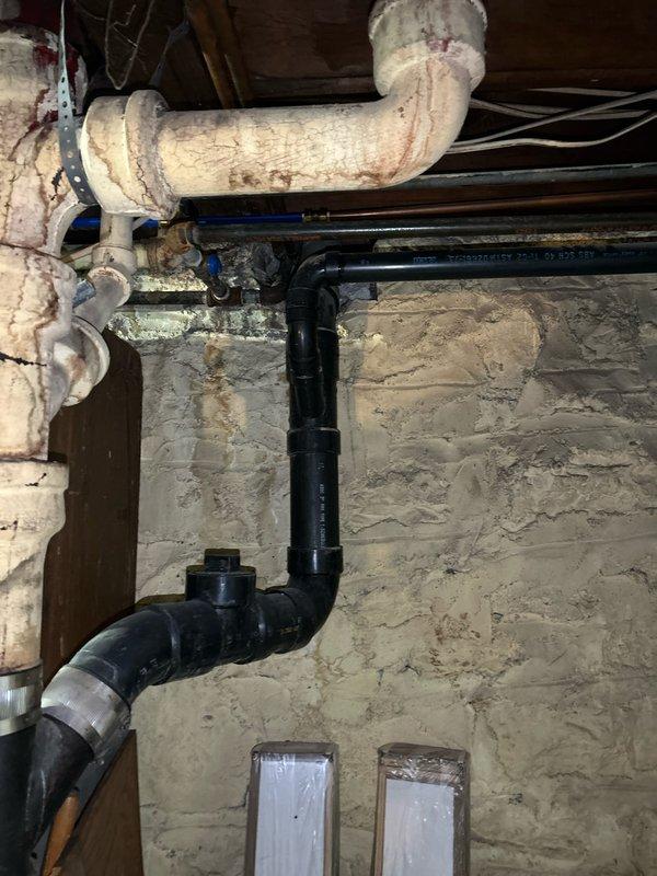 Responded to kitchen sink clog potentially originating from dishwasher connection. Upon inspection, accessed basement plumbing infrastructure beneath affected fixture and examined drainage system including black PVC vertical drain lines and associated horizontal waste piping. Verified proper venting configuration and assessed condition of drain connections at floor joist level where kitchen plumbing tie-ins are located.