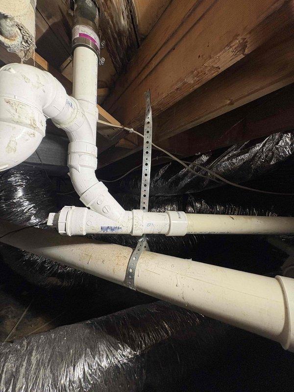 Responded to a recurring bathtub clog that had not been fully resolved by previous snaking attempts. Accessed the crawl space beneath the residence to inspect the drainage system and replaced deteriorated PVC piping sections. Installed new white PVC pipe assembly with proper joints, elbows, and secure metal strapping brackets to the floor joists to ensure proper drainage flow and prevent future blockages.