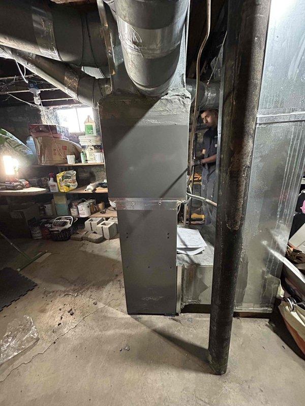 Completed full HVAC system replacement in residential basement, installing RUUD R801T0503A14UHSNAS 50,000 BTU 80% efficiency gas furnace, RA14AY30AJ1NALHP 2.5 ton 14.3 SEER2 air conditioning unit, and RCFY3617STANMC 2.5 ton evaporator coil. Removed existing equipment and properly disposed of old system components. Set new furnace on ground level using isolation pads, removing previous blocking. Centered evaporator coil on furnace and fabricated custom sheet metal blocking for side gaps to ensure proper fit and airflow. 

Installed outdoor condensing unit on new equipment pad with electrical whip kit and disconnect box for code compliance. Ran and insulated refrigerant lines between indoor and outdoor units, installing filter drier in refrigerant circuit. Fabricated transition ductwork connecting evaporator coil to existing duct system using insulated metallic ductwork. Installed SS2 condensate safety switch with water sensor on drain line as secondary overflow protection. Connected con