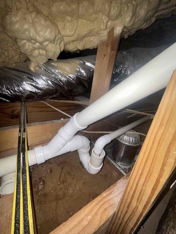 # Attic Drain Line Repair

Responded to clogged drain issue in attic crawl space. Upon inspection, identified defective tee fitting in main drain line causing blockage and potential backup. Accessed confined attic space through existing entry point and navigated around HVAC ductwork and insulation to reach affected plumbing system.

Removed damaged PVC tee fitting and surrounding compromised pipe sections. Cleared debris and buildup from drain line to ensure proper flow. Installed new PVC tee fitting with appropriate elbow connections, ensuring proper pitch and alignment for optimal drainage. Secured all joints with primer and PVC cement per code requirements. Tested system for leaks and verified proper water flow through repaired section.

Confirmed no moisture damage to surrounding wooden structural members or insulation. Restored work area and removed all debris. System operational and draining properly upon completion.