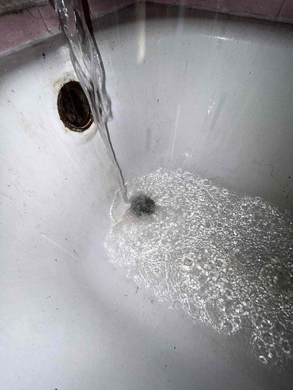 Responded to service call for slow-draining bathroom sink and hissing toilet tank in early 1970s home where issues had persisted for approximately one month. Inspected bathroom plumbing fixtures and identified partial blockage in sink drain causing delayed drainage. Cleared obstruction from sink drain line using appropriate drain cleaning equipment, restoring proper water flow. Examined toilet tank components and located source of hissing sound, which was determined to be a faulty fill valve allowing continuous water seepage. Replaced defective fill valve assembly with new unit to eliminate air leak noise and prevent water waste. Tested both fixtures after repairs to verify proper operation—sink now drains at normal rate and toilet tank fills quietly without hissing. Documented conditions with photographs showing vintage pink tile bathroom with chrome fixtures and sink drainage test confirming restored functionality.