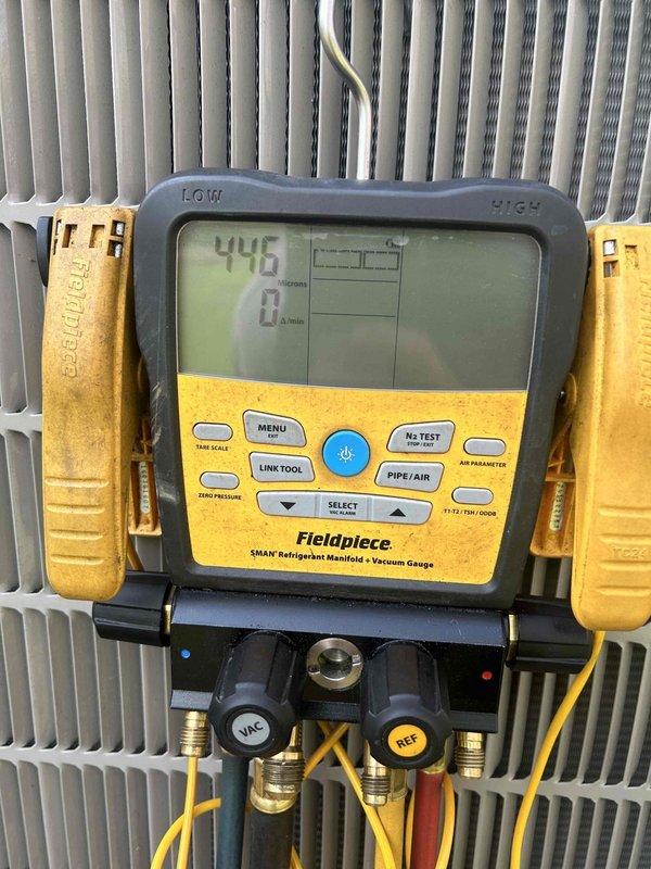 Performed electronic leak search on HVAC system using Fieldpiece SMAN refrigerant manifold and vacuum gauge. Connected diagnostic equipment to R-410A system and monitored refrigerant pressures, recording 128.9 psig on low side and 276.7 psig on high side at 84°F ambient temperature to identify leak location within the condenser unit.