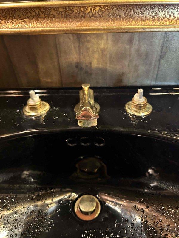 Responded to dripping faucet in half bath. Disassembled ornate brass three-piece faucet assembly with porcelain handles mounted on black countertop. Replaced worn valve cartridges and internal seals that were causing the drip. Reassembled faucet, tested both hot and cold water controls, and verified complete elimination of leak with no dripping present.