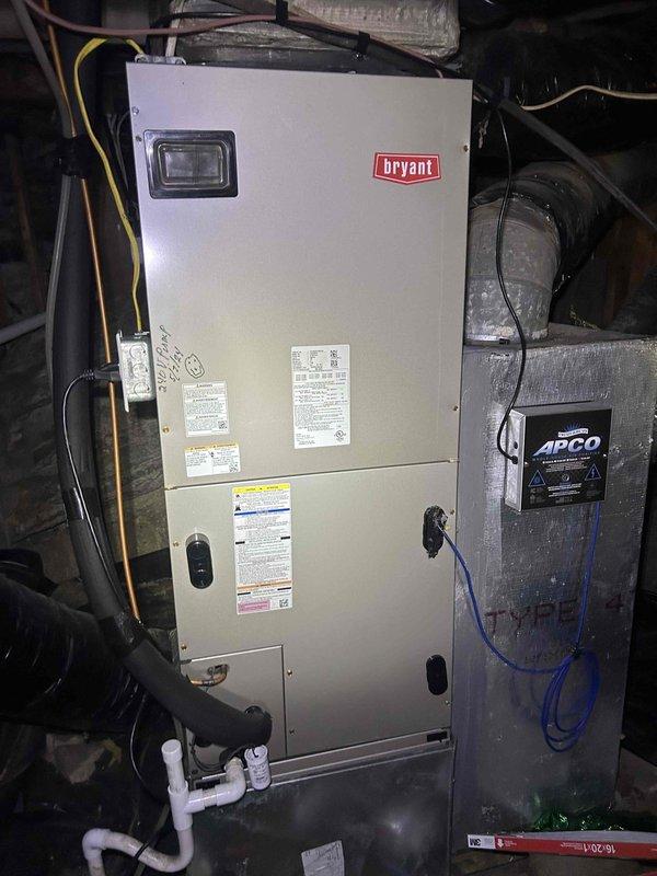 Responded to no cool call on electric heat pump system with indoor air handler located in walkout basement. Upon arrival, customer reported system not reaching thermostat setpoint. Performed visual inspection of Bryant indoor air handler unit and outdoor condensing unit. Observed outdoor condenser positioned on ground level adjacent to wooden deck with weathered surrounding area. Indoor unit installation appeared standard with proper electrical connections, PVC condensate drainage, and APCO air purification device installed on ductwork. Checked system operation and airflow at indoor unit. Documented equipment condition through photographs for service records. System requires further diagnostic testing to determine root cause of insufficient cooling capacity and inability to satisfy thermostat demand.