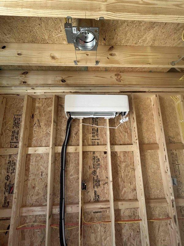 Completed installation of Friedrich 9K BTU mini split heat pump system in residential property under construction. Installed FPHSR09A3D outdoor condensing unit on exterior wall bracket and FAHFW09A3D indoor wall-mounted air handler with refrigerant line set, electrical whip kit, disconnect box, and insulated refrigerant lines. System tested and operational; documentation photographed including equipment model and serial number tags per protocol.