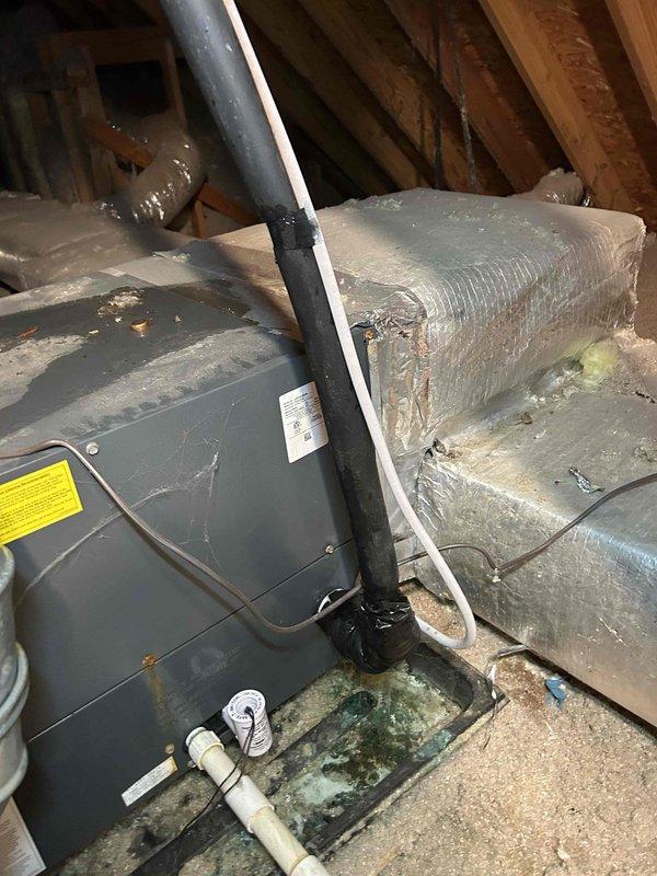 Responded to no cooling call on electric HVAC system with air handler located in attic. Upon inspection, found standing water in condensate drain pan with visible debris accumulation, indicating potential drain line blockage affecting system operation. Documented attic-mounted air handler unit and flexible ductwork installation, noting insulation condition and PVC condensate drain configuration with proper trap assembly. Photographed equipment nameplate for age verification and captured drain pan condition showing sediment buildup in standing water. System evaluated for repair versus replacement recommendation given age of equipment exceeding ten years.