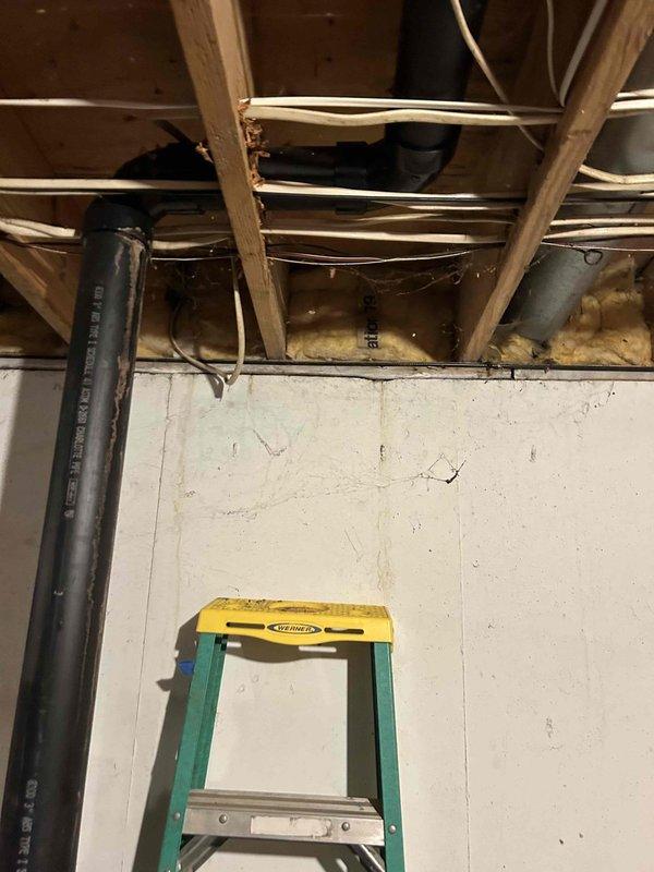 Completed sump pump relocation assessment and planning for basement drainage system. Evaluated existing sump pump discharge routing and confirmed feasibility of rerouting discharge line to front yard with placement beyond sidewalk as requested. Inspected basement ceiling structure, existing plumbing infrastructure, and discharge piping configuration to determine optimal path for new discharge line installation. Documented current system setup including exposed joists, existing pipe runs, and available routing options through photographic evidence. Prepared specifications for permanent relocation work to ensure proper drainage away from foundation while meeting municipal requirements for LFUCG compliance.